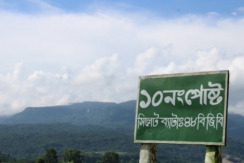 a large green sign with writing written in front of a mountain