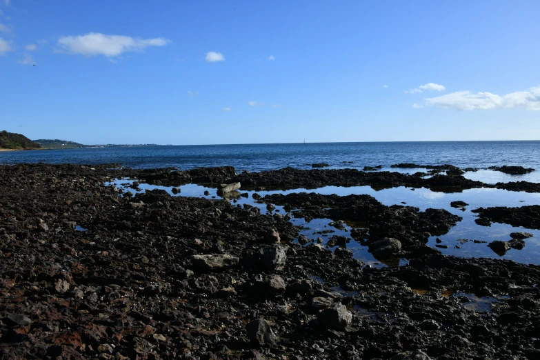 a lone kite is flying over the rocks on a beach