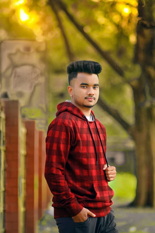 an indian man in plaid shirt and cap standing near trees