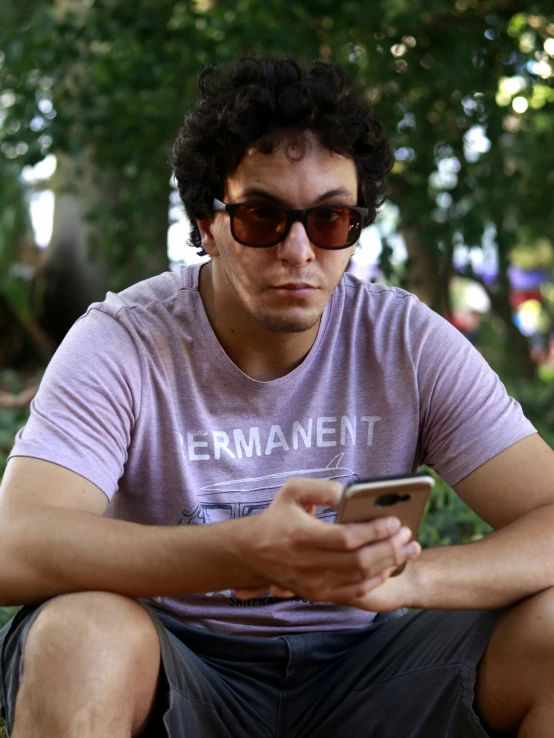 a man in sunglasses sitting on the ground with a cell phone