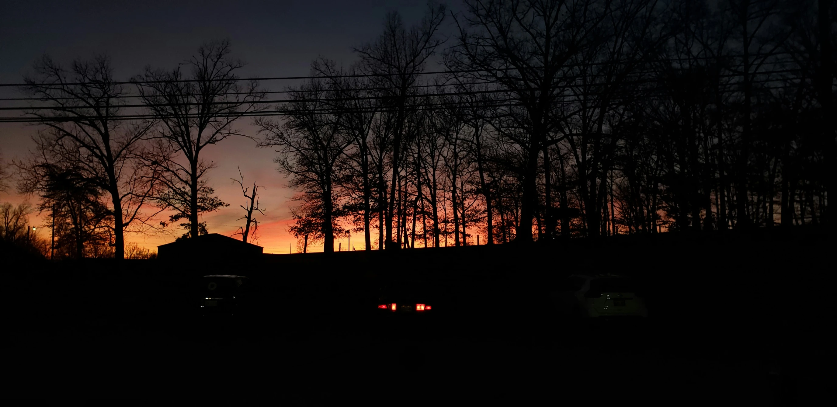 a dark picture shows the setting sun over trees and a small farm