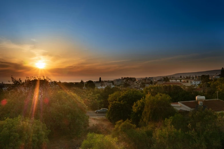 the sun sets over the town beyond a forest filled city