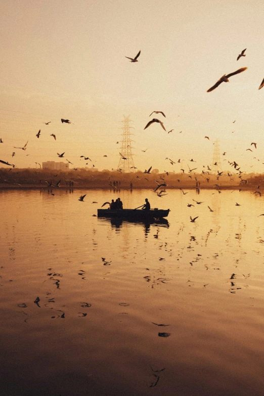 a man paddling his boat in a lake with many birds flying around