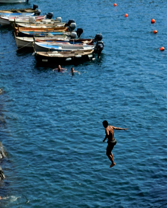 a person jumping in the water near boats