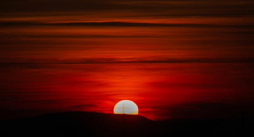 a large bright orange and red sun behind some small hills