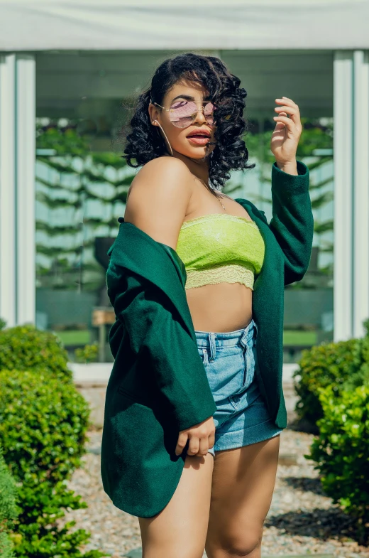 a woman wearing a green jacket and denim shorts