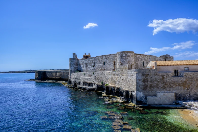 an old stone building on the water by a pier