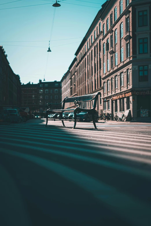 two park benches in the sun near a row of buildings