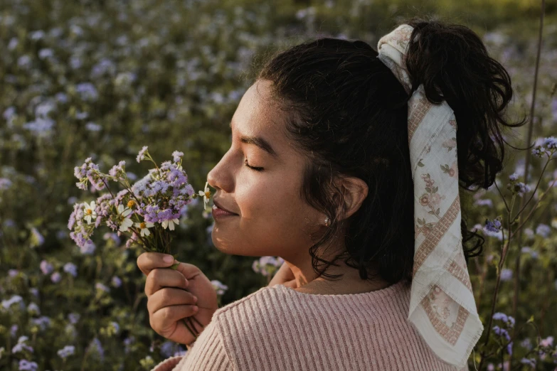 a girl in a field of flowers holding on to a floral arrangement