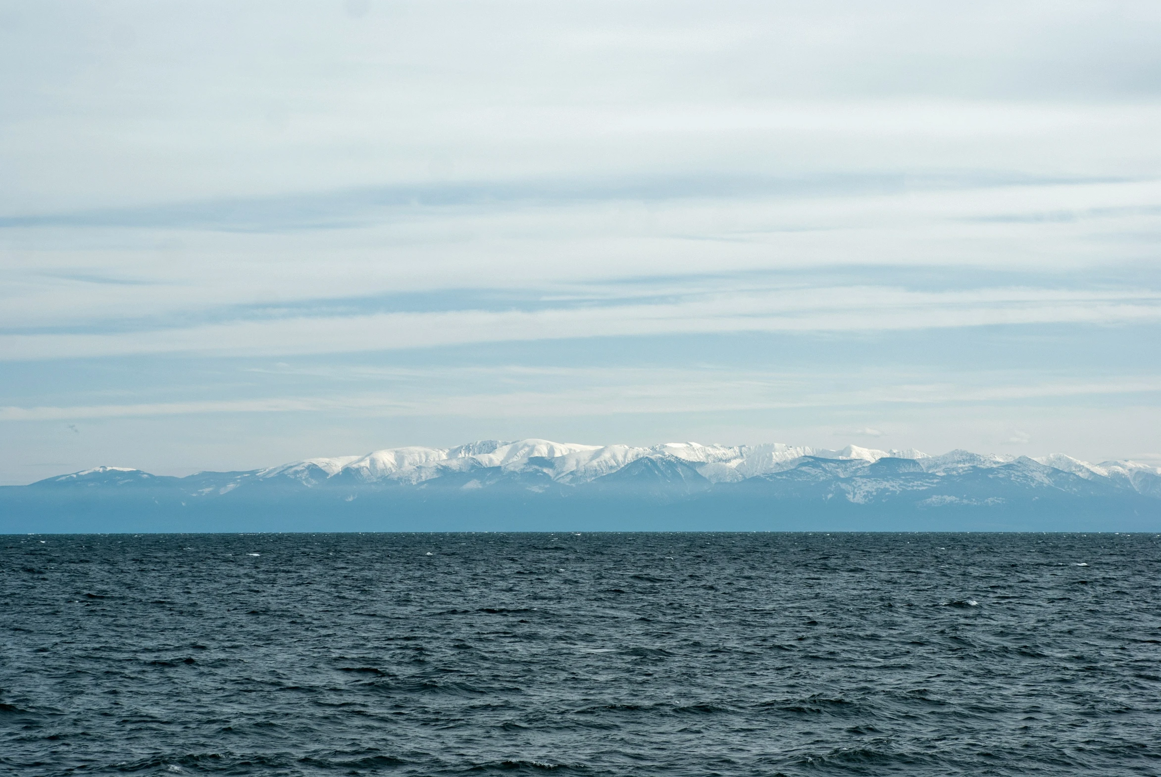 a sailboat in the ocean with snowy mountains in the background