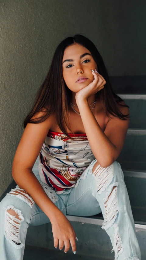 a young woman wearing torn jeans poses on the stairs