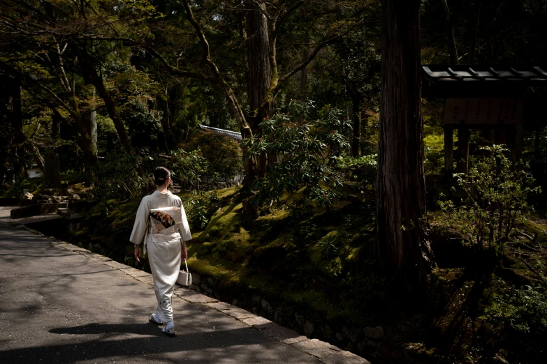 a woman in a white robe carrying a bag walking along a path