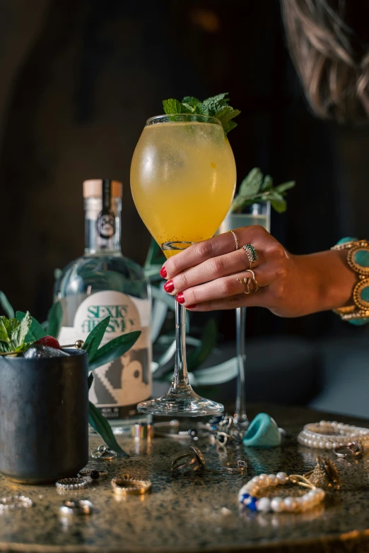 a woman holds a drink next to a plant in a vase