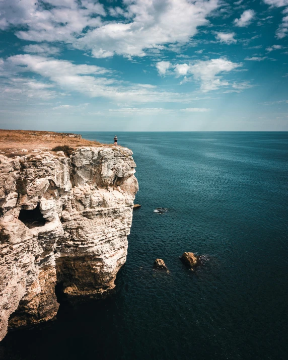 a person is standing on the edge of an cliff on the ocean