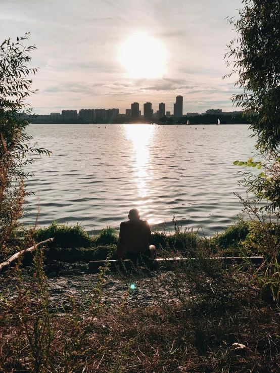 a man sitting by the river with the sun peeking through