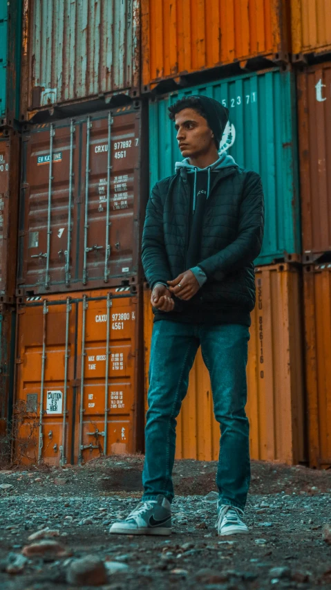 a man standing by a fence with lots of shipping containers behind him