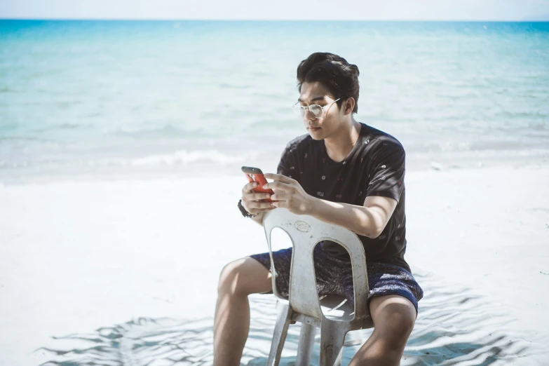 man sitting on a chair at the beach using a cell phone