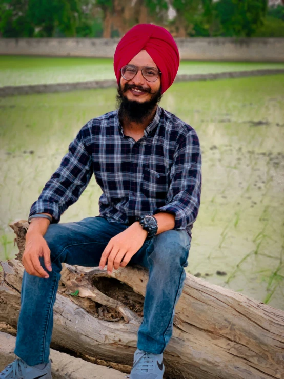 man sitting on tree nch wearing blue jeans and a red turban