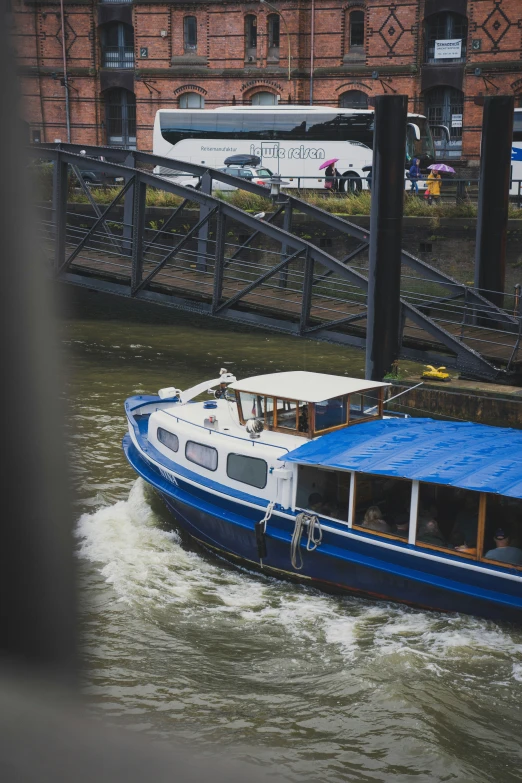 a blue boat moving down a river under a bridge