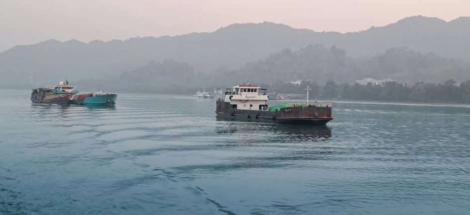 two tug boats in the water with mountains behind them