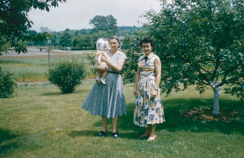 two women pose for a po in front of an apple tree