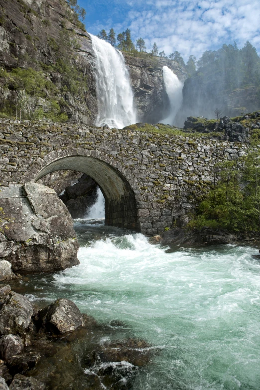 the waterfall runs under an old stone bridge