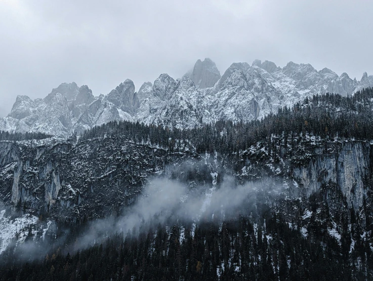 the mountain range is covered with snow and low fog