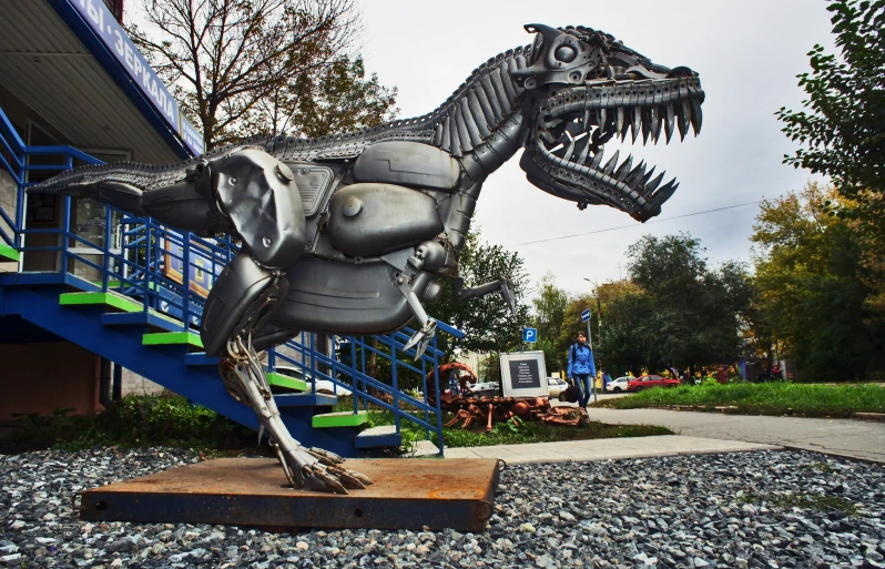 a metal dinosaur statue standing on display outside of a building