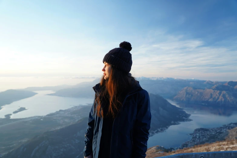 a young woman looks down at the water from the top of a mountain