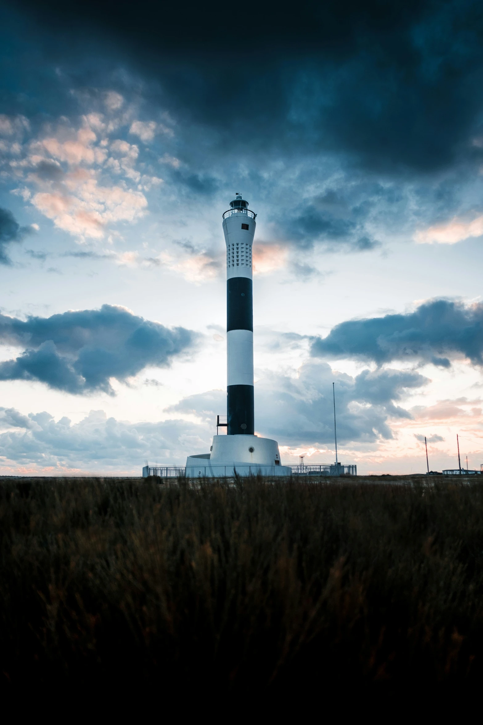 a lighthouse sits in a grassy field under clouds