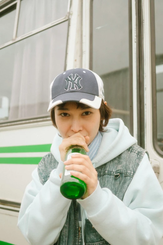 a girl drinking beer standing in front of a bus