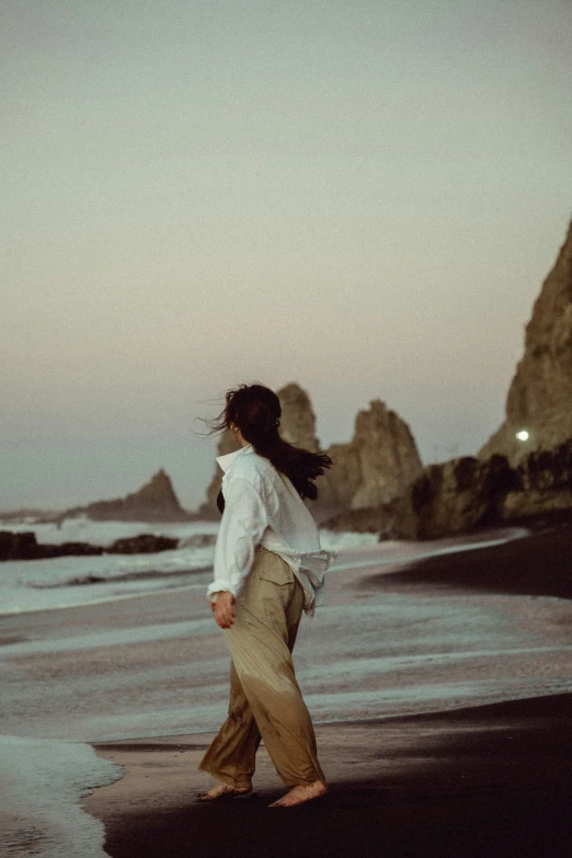 a woman walking along the water in front of some rocks