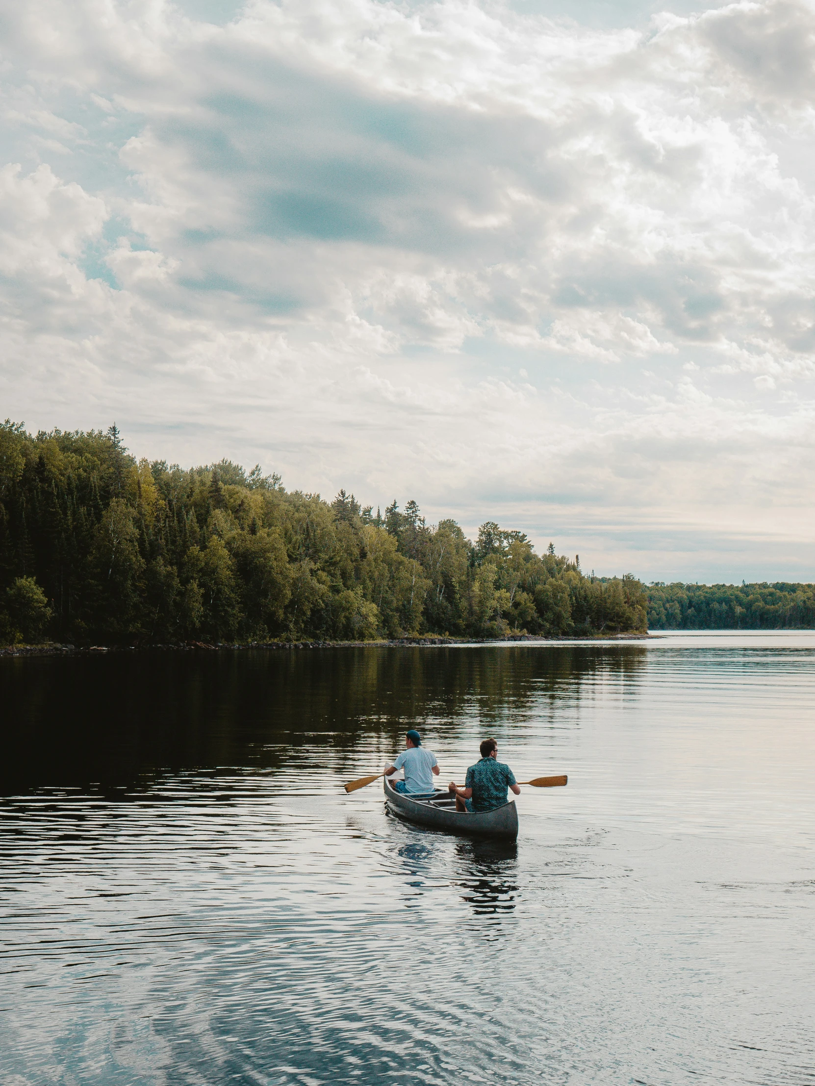 two people in a canoe out on a river with a forest behind them