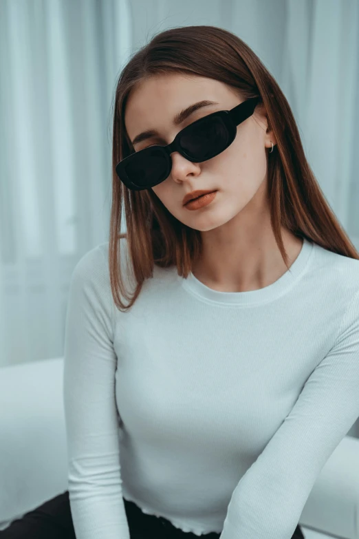 a girl sitting on a bed wearing a pair of sunglasses