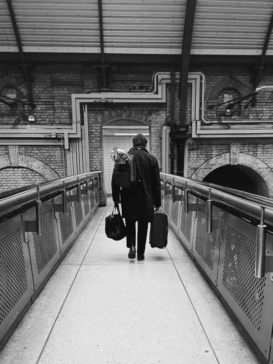 man with two suitcases walking across a bridge