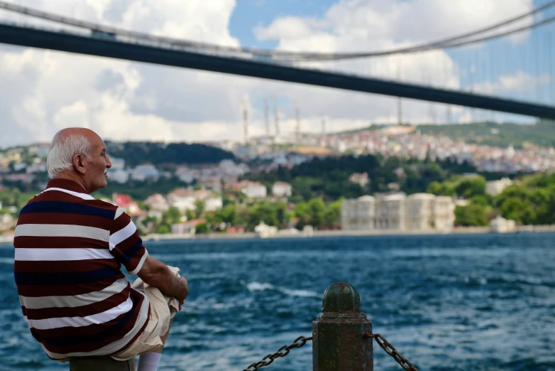 man sitting on post watching the river with bridge in the background