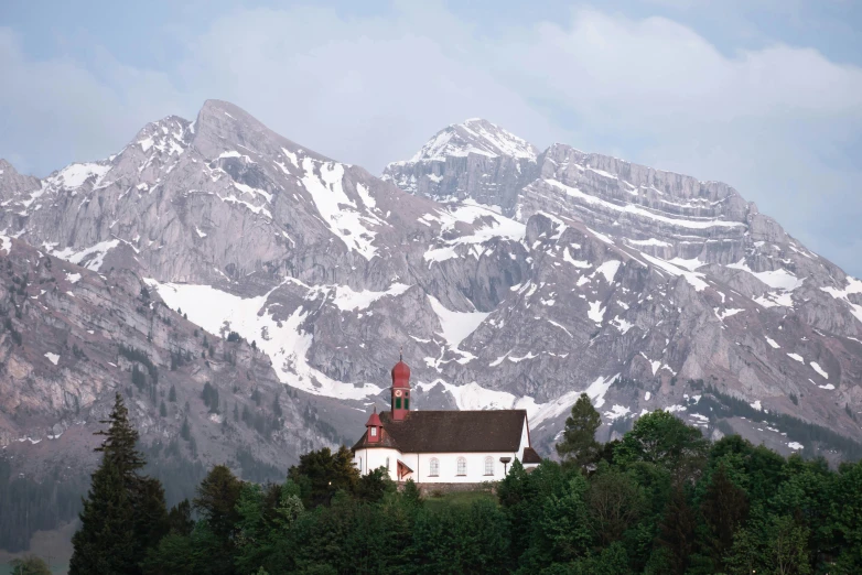 a large mountain range in the distance with a white church building and a brown roof