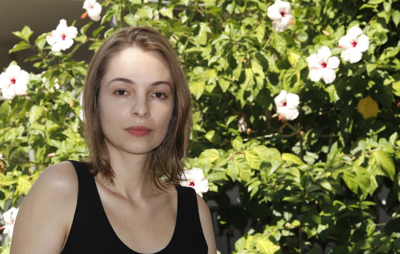 a woman with brown hair and a black tank top standing in front of a tree