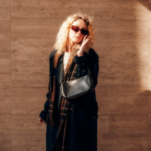 a beautiful young woman holding a purse near a wall