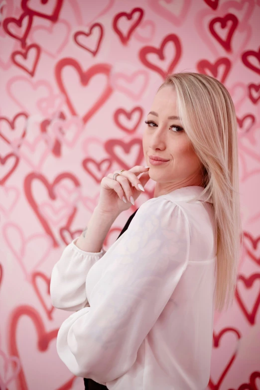 a beautiful blonde lady in a white shirt standing in front of pink hearts