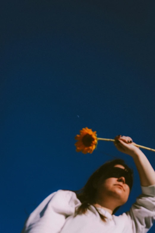 a woman standing under a blue sky holding a single flower