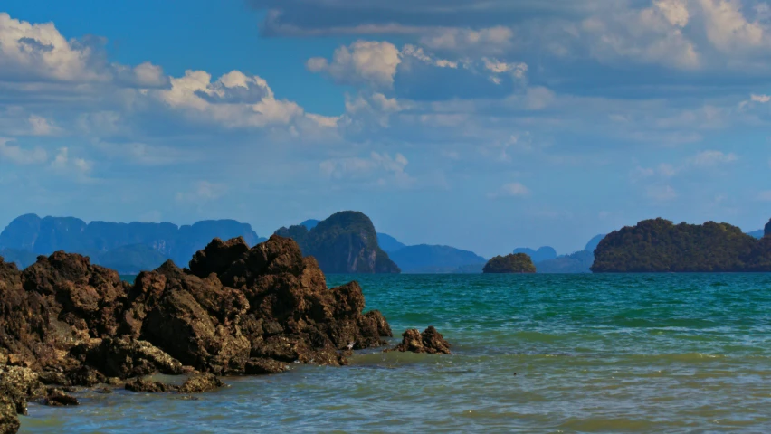 people walking along the beach by some rocks