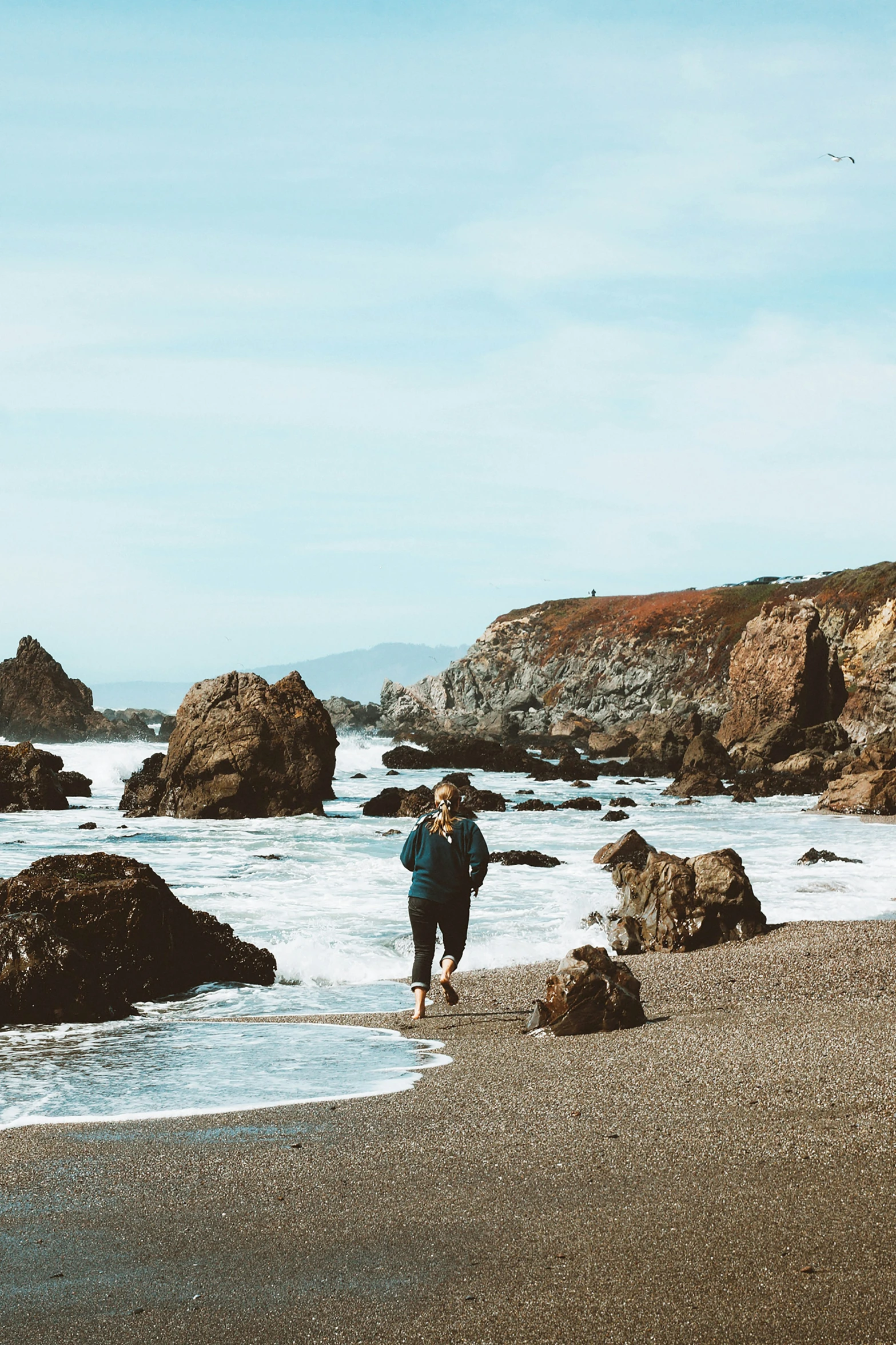 a woman is standing on the beach looking at her cell phone