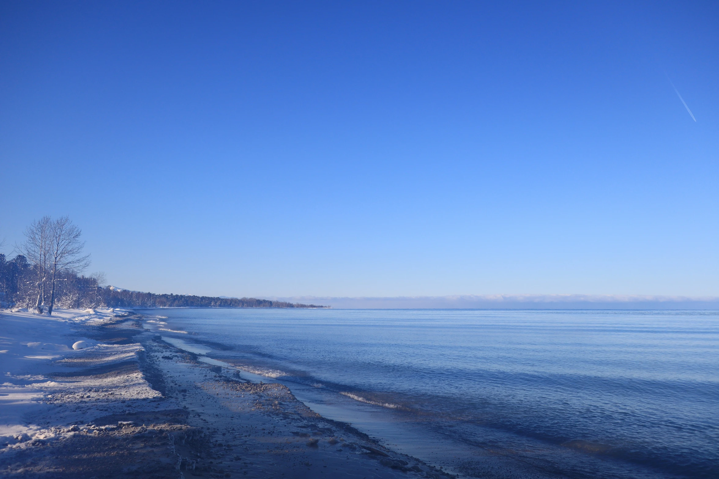 a clear blue sky and some ice water and trees