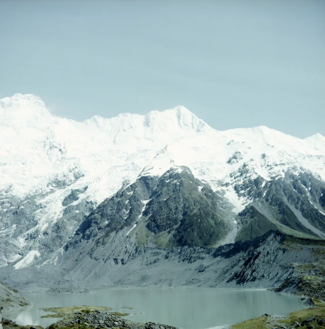 an mountain with snow on top sitting in the middle of a field