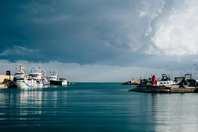 boats are docked at the ocean side with grey skies