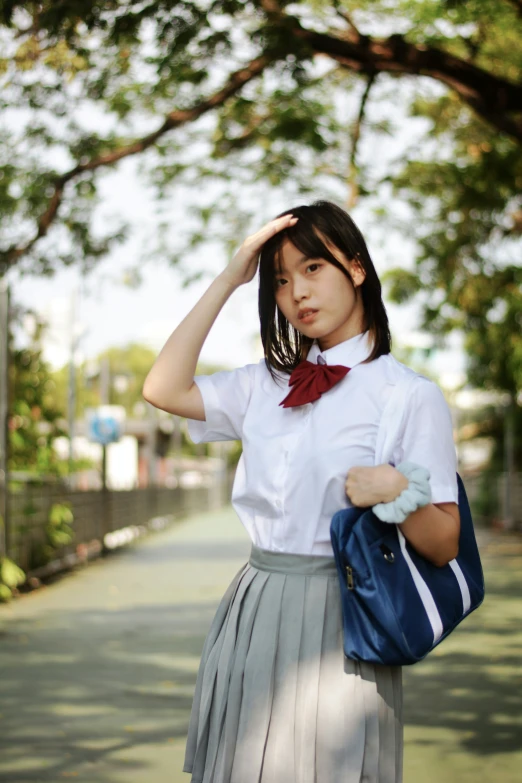 a woman in white shirt and grey pleated skirt with a blue hand bag