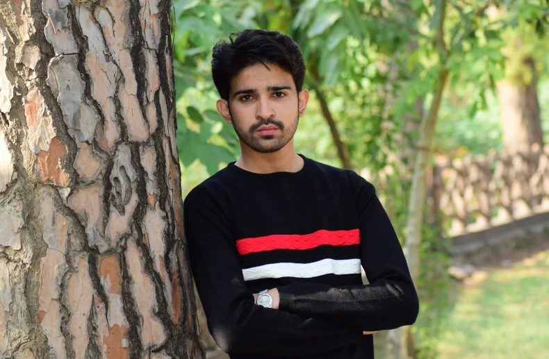 a young man leans against a tree in the woods