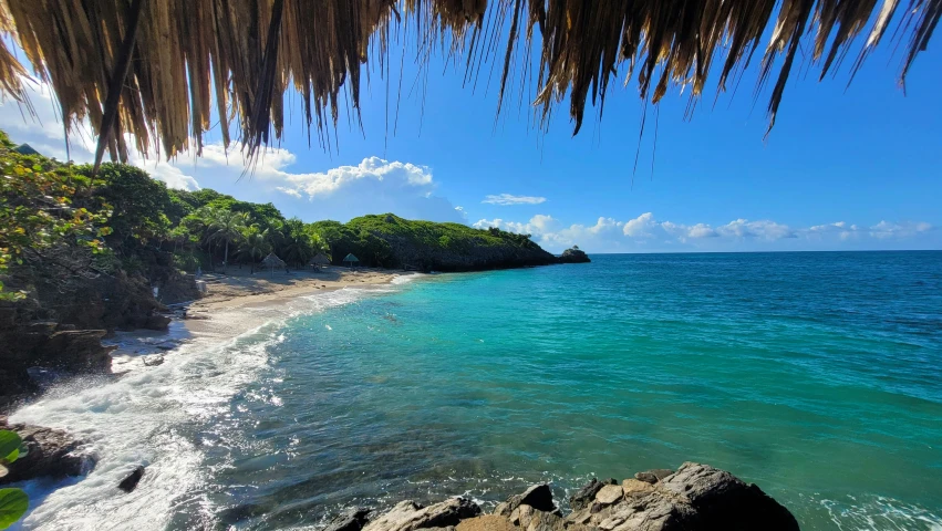 an empty tropical beach under a thatched roofed umbrella