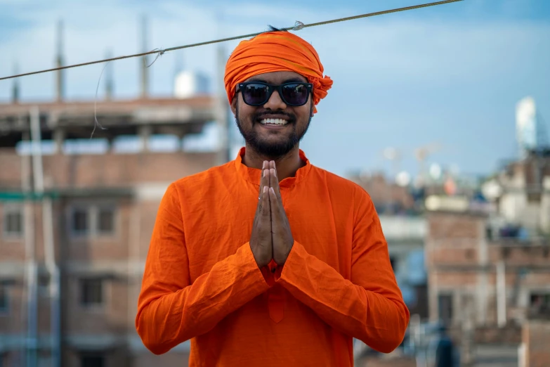 a man smiling with his hands together and an orange turban covering his face